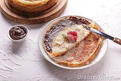 Plate with delicious thin pancakes, raspberries and chocolate paste on light table Stock Photo