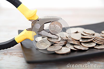 A plate of dollar coins and a pair of pliers holding a coin Stock Photo