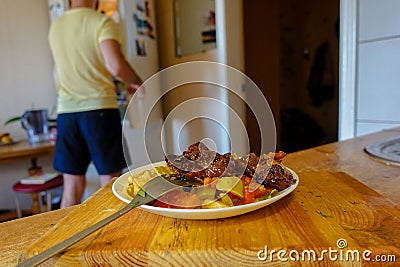 A plate of food on the table. In the background, a man opened the refrigerator Stock Photo