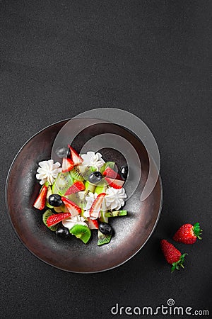 Plate with fruit salad, kiwi, strawberries, blueberries, apple, whipped cream Stock Photo