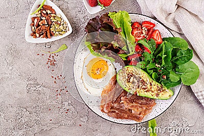 Plate with a keto diet food. Fried egg, bacon, avocado, arugula and strawberries. Stock Photo