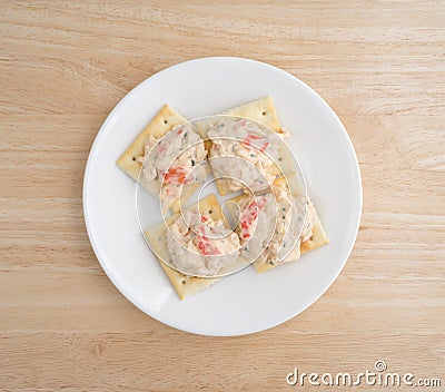 Plate of lobster dip on saltine crackers atop wood table Stock Photo