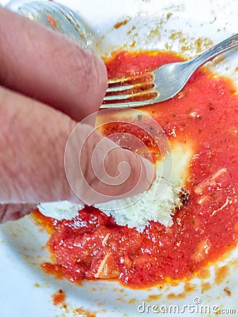 Plate of pasta just finished with hand cleaning the remaining tomato with a piece of bread. Stock Photo