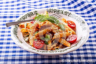 Plate with pasta pene Bolognese sauce cherry tomatoes parsley top and basil leaves on checkered blue tablecloth. Stock Photo