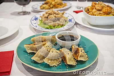 Plate with a portion of gyozas cooked on the grill, dim sum, with soy sauce, poppy seeds and sesame on a blue plate of a Chinese Stock Photo