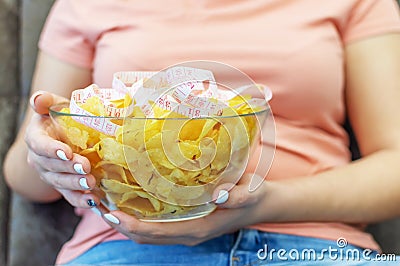 A plate of potato chips and a centimeter tape in the girl`s hands. Junk food. The concept of struggle against excess weight. Stock Photo