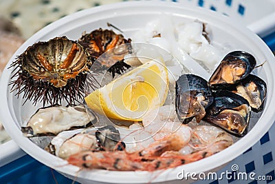 Plate of raw fresh sea fruit or food, ready to eat with sea urchins, prawns, shrimps, oysters, black mussels, cuttlefish and lemon Stock Photo