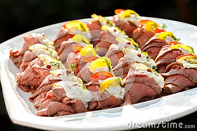 Plate of sliced, rolled and garnished roast beef canapes. On black background. Stock Photo