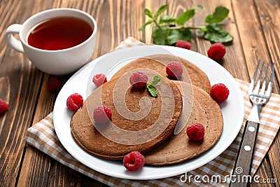 Plate with tasty chocolate pancakes, raspberries and cup of tea on wooden table Stock Photo