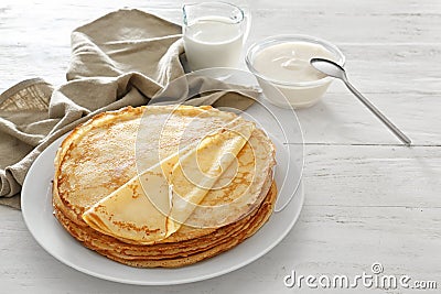 Plate with tasty thin pancakes, sour cream and jug of milk on wooden table Stock Photo