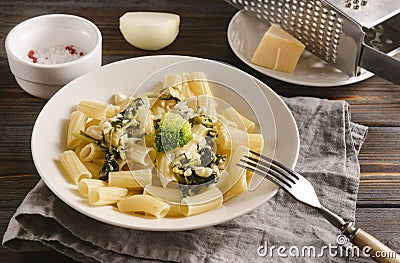 Plate with tortilloni with sauce and spinach and cheese, broccoli, fork, napkin, cheese grater on a light background, spinach Stock Photo