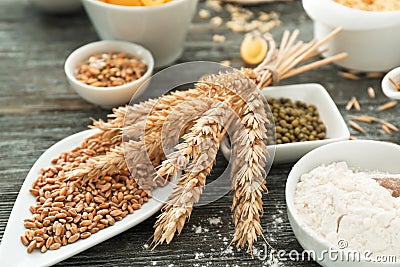 Plate with wheat grains, spikelets and flour on wooden table Stock Photo