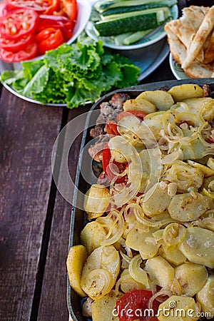 Plates with chopped tomatoes, cucumbers and a dish with baked potatoes Stand on a wooden table Stock Photo