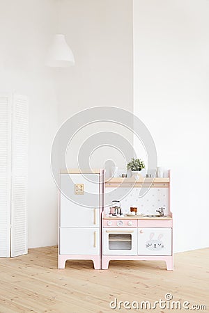 Play furniture for children. Wooden pink and white kitchen with fridge, stove, oven and sink in big light room Stock Photo