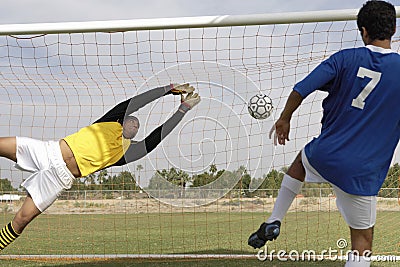 Player Scoring Goal While Goalkeeper Diving To Save It Stock Photo