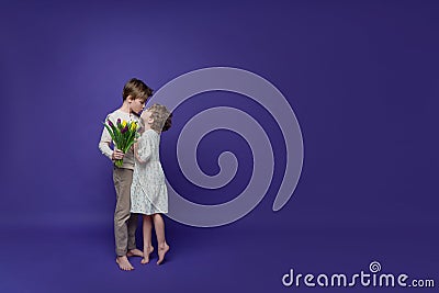 Playful friendly kiss of two cheerful children, boy and girl, dressed in beige casual clothes, with tulips in their hands on Stock Photo