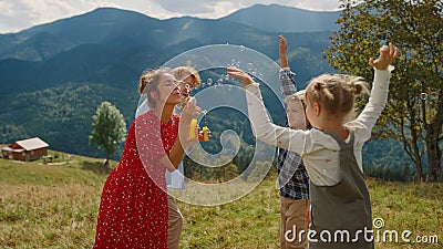 Parents blowing soap bubbles on green meadow. Children catching bubbles outdoors Stock Photo