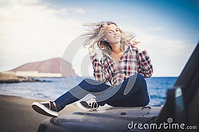 Playful young attractive blonde play with the wind sitting on his car and enjoying the travel alternative adventure vacation alone Stock Photo