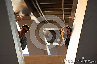 Playful young couple posing in urban space hiding looking out of bridge waving hands happy smiling Stock Photo