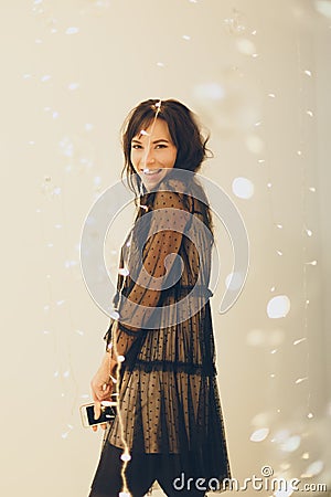 Playful young woman in cocktail dress staying smiling over lights background Stock Photo