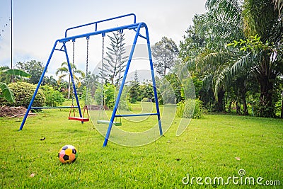 Playground equipment in the backyard for kids with soccer goal net and football on green grass field background. Stock Photo