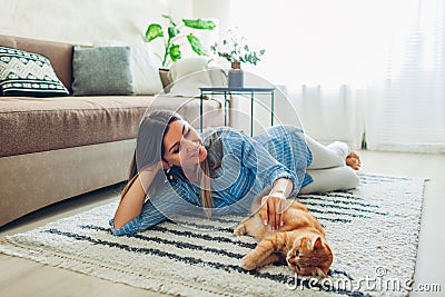 Playing with cat at home. Young woman lying on carpet and teasing pet Stock Photo