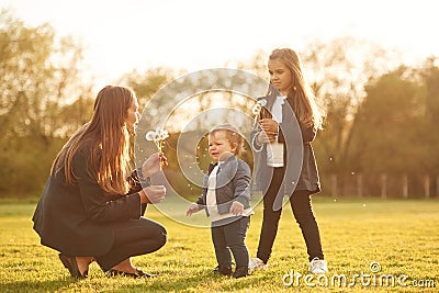 Illuminated by sunlight. Playing with dandelion. Woman with her two young daughters is on the summer field Stock Photo