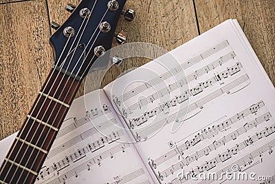 Playing guitar... Close-up photo of guitar neck and music notes against of wooden background. Stock Photo