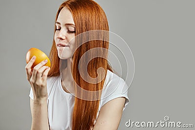 Pleasant ginger woman in white T-shirt is tasting the fruit Stock Photo