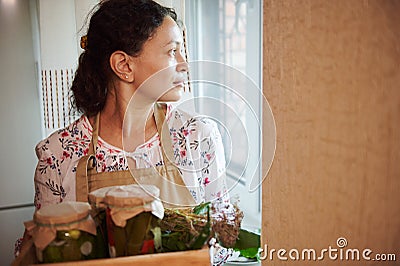Pleasant looking through the window, holding box with jars of pickled vegetables, preserved according to homemade recipe Stock Photo