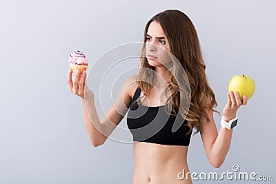 Pleasant puzzled woman holding fruit and cupcake Stock Photo