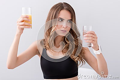 Pleasant puzzled woman holding glasses of water and juice Stock Photo