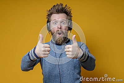 Pleasantly surprised man in headphones listens to music and makes an approving gesture, thumbs up. Yellow background. Stock Photo