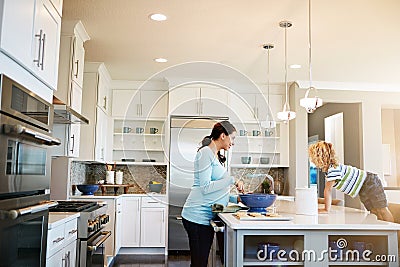 Please add extra chocolate chips to the cookies, Mom. a little boy watching his mother bake cookies at home. Stock Photo