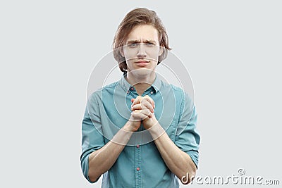 Please help me. Portrait of hopeful handsome long haired blonde young man in blue shirt standing with palm hand and hope for help Stock Photo