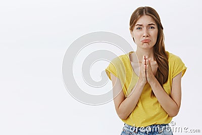 Please I need your help. Portrait of silly cute whining girl in yellow t-shirt holding hands in pray pursing lips as if Stock Photo