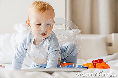 Pleased blonde baby boy looking at tablet computer while playing on bed Stock Photo