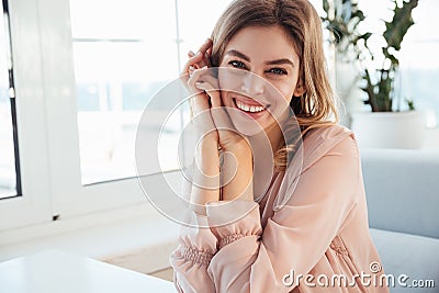 Pleased blondy woman in blouse sitting by the table Stock Photo