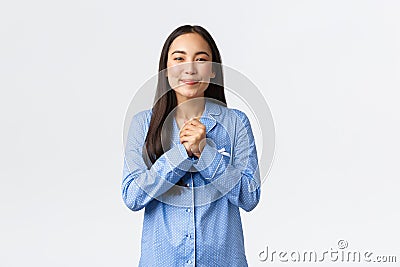 Pleased and delighted asian girl in blue pajamas holding hands together clasped and smiling satisfied, gladly receive Stock Photo