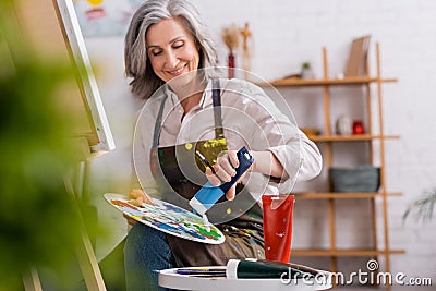 pleased mature artist pouring blue paint Stock Photo