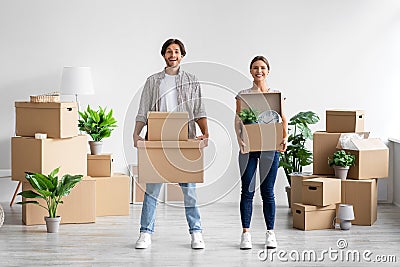 Pleased millennial caucasian male and female carry boxes and plants in room interior and enjoy moving at own home Stock Photo