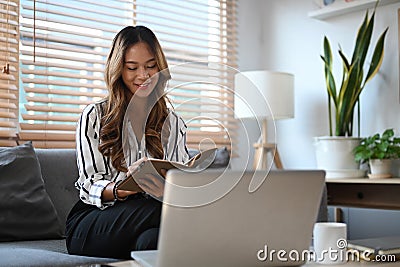 Pleased woman sitting on couch and reading book. Stock Photo