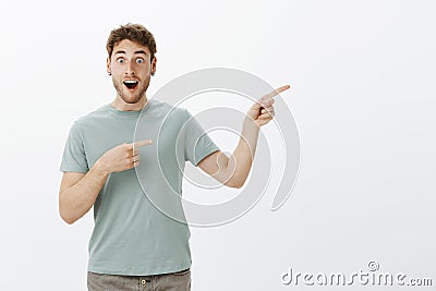 Pleased surprised attractive guy with fair hair, dropping jaw while discussing something amazing, pointing right with Stock Photo