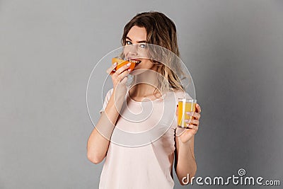 Pleased woman in t-shirt eating orange while holding juice Stock Photo
