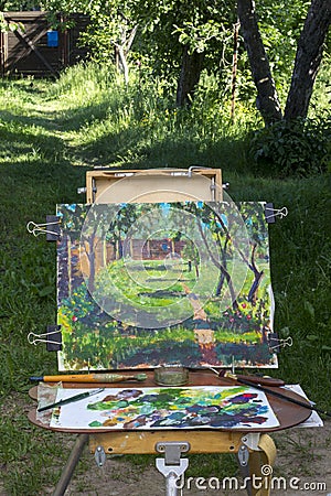 Plein air in nature. Canvas on sketchpad, a palette with used paints. Stock Photo