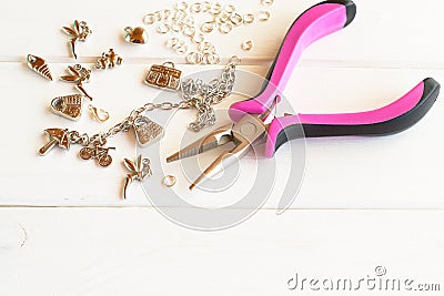 Pliers, chain, metal rings and pendants on a white wooden background. How to do yourself metal bracelet Stock Photo