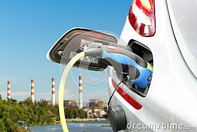 Plug of power cable electric supply during charging at ev car electric vehicle charging on electric power plant with smokestack Stock Photo