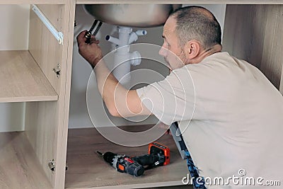The plumber connects the faucet to the plumbing, installing sink in new kitchen Stock Photo