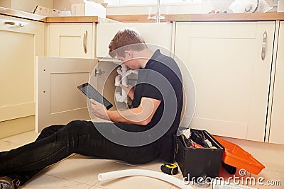 Plumber fixing sink in kitchen consulting tablet computer Stock Photo