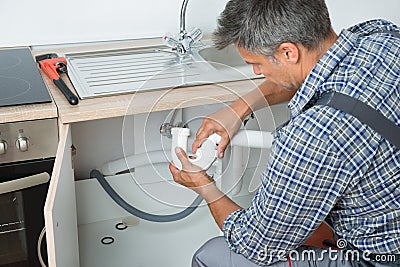 Plumber Fixing Sink Pipe In Kitchen Stock Photo